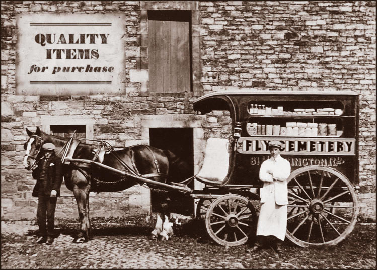 Dark sepia photograph of a stationary horse and wagon, a window in the side of the wagon reveals various bottles, jars, boxes and bags lined up on two shelves.  On the wall behind the horse and wagon is a sign bearing the text: Quality Items for Purchase