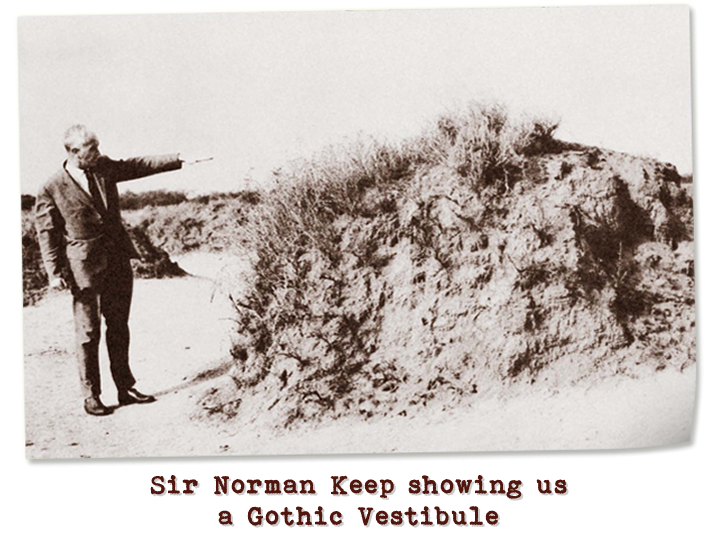 Black and white photograph of an older gentleman pointing towards a dirt mound partially covered with grass.  Captioned: Sir Norman Keep showing us a Gothic Vestibule